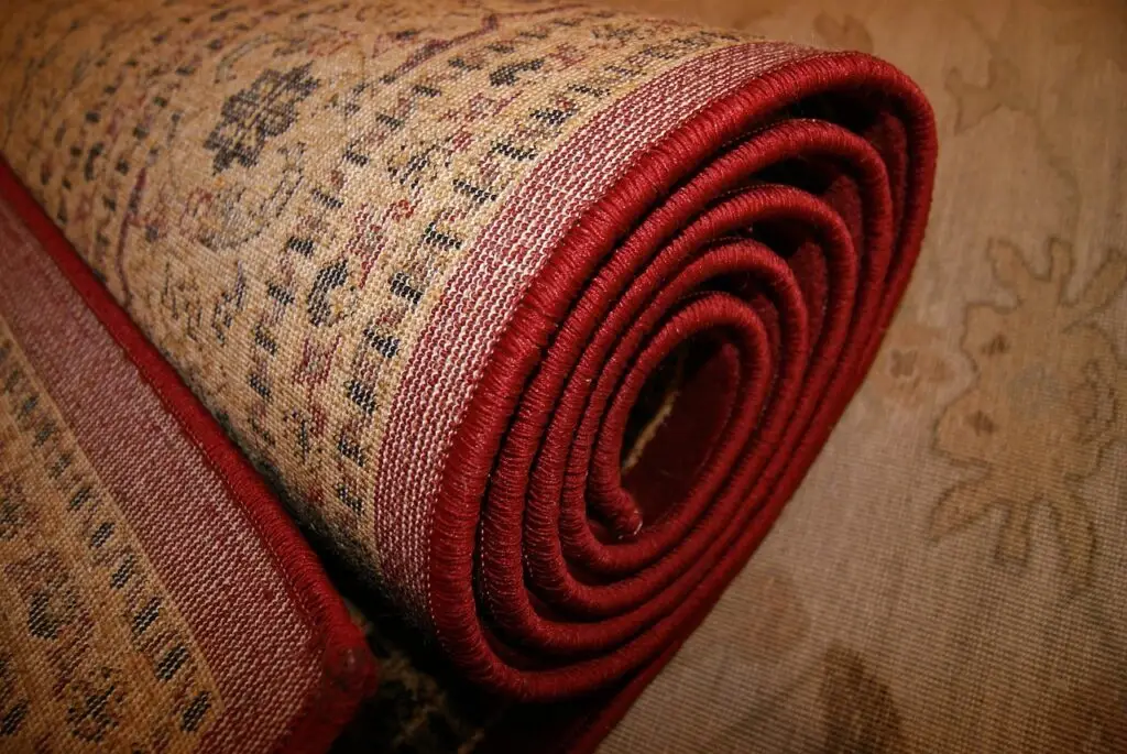 Rolled-up traditional area rug with red trim, highlighting the detailed woven texture and patterns. A quality rug pad underneath can help protect floors and extend the rug’s lifespan.