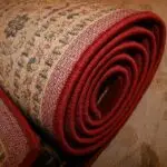 Rolled-up traditional area rug with red trim, highlighting the detailed woven texture and patterns. A quality rug pad underneath can help protect floors and extend the rug’s lifespan.