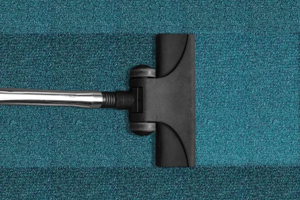 Close-up of a vacuum cleaner on a teal carpet, highlighting the importance of keeping area rugs professionally cleaned for improved hygiene and longevity